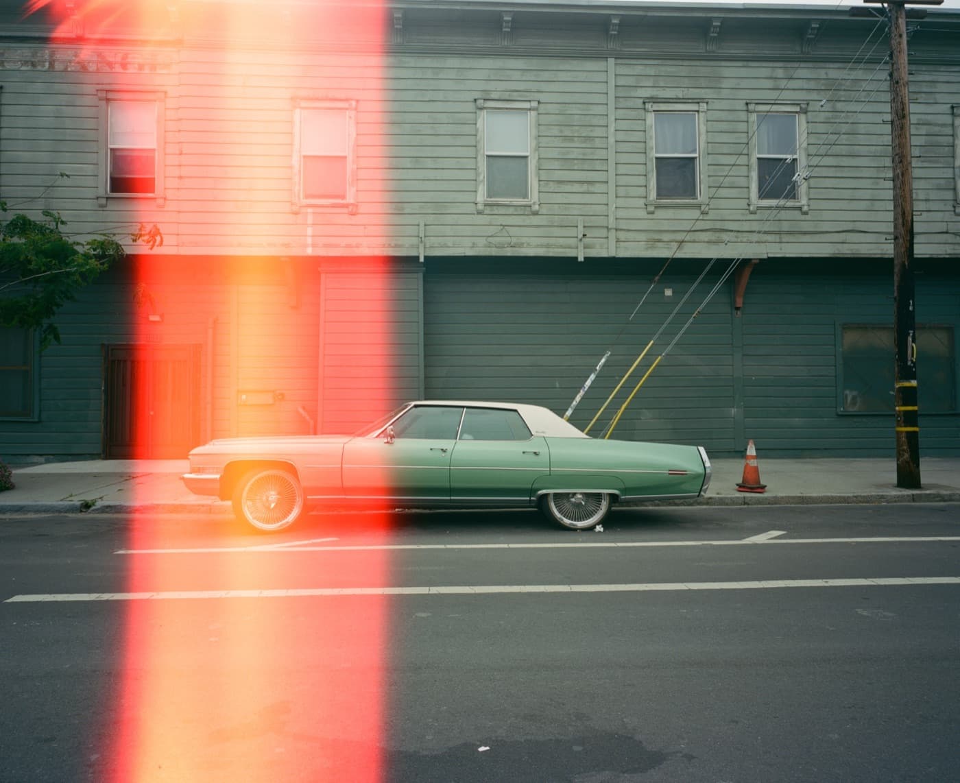Film photograph — light leak over a green Cadillac on a quiet street